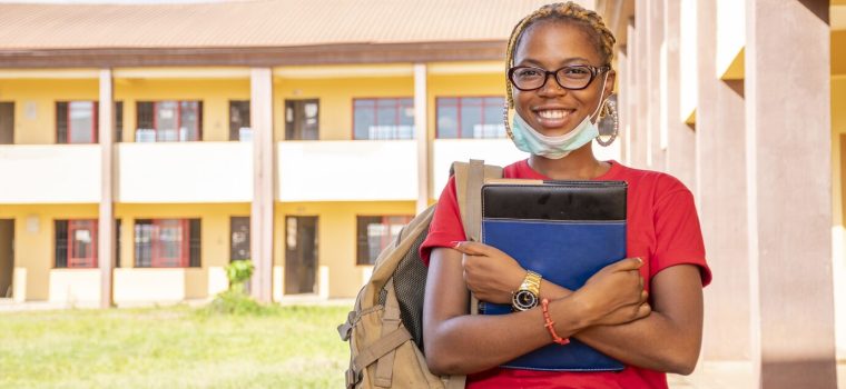 young-african-female-student-with-facemask-holding-her-textbooks-campus-area_181624-41232